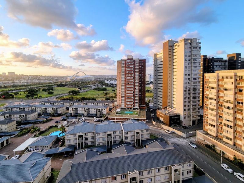 An elevated aerial view of the surrounding urban landscape, featuring high-rise apartment buildings, residential complexes, and a distant stadium under a clear sky.