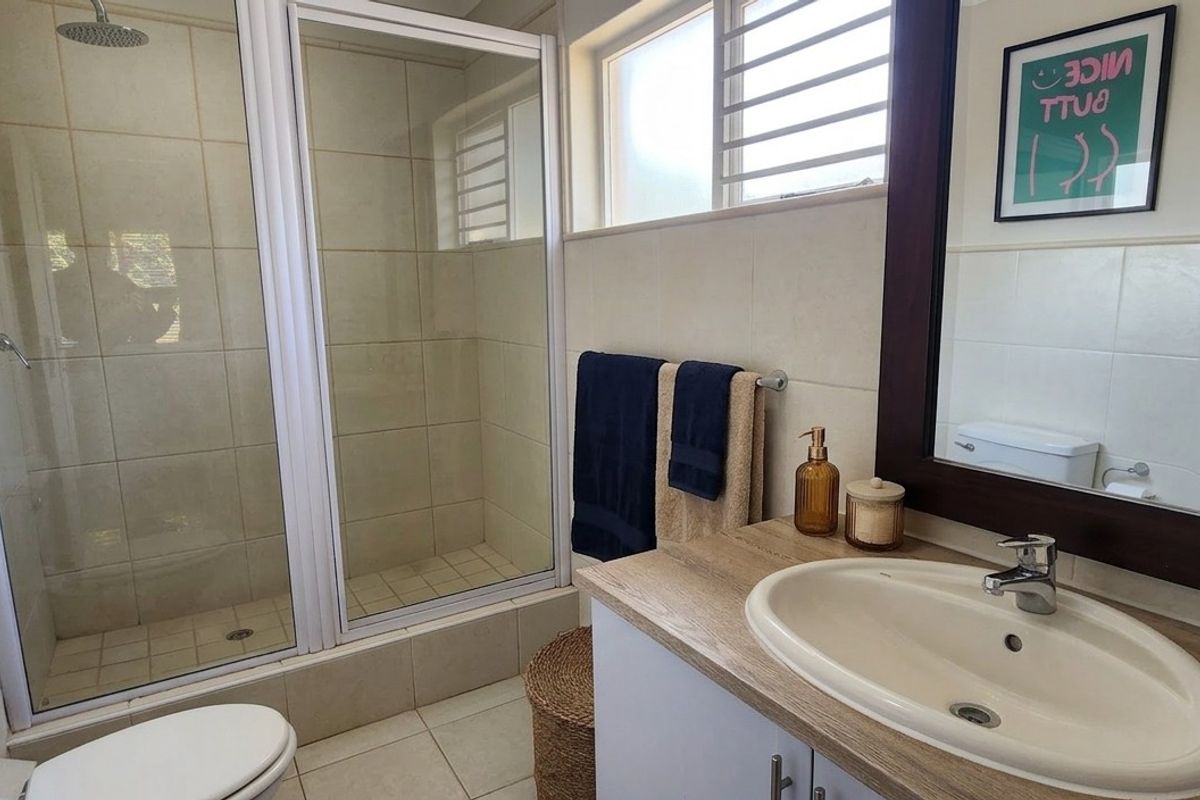 A functional bathroom featuring a tiled shower enclosure with a rain shower head, a vanity with a basin, and a wall-mounted mirror.