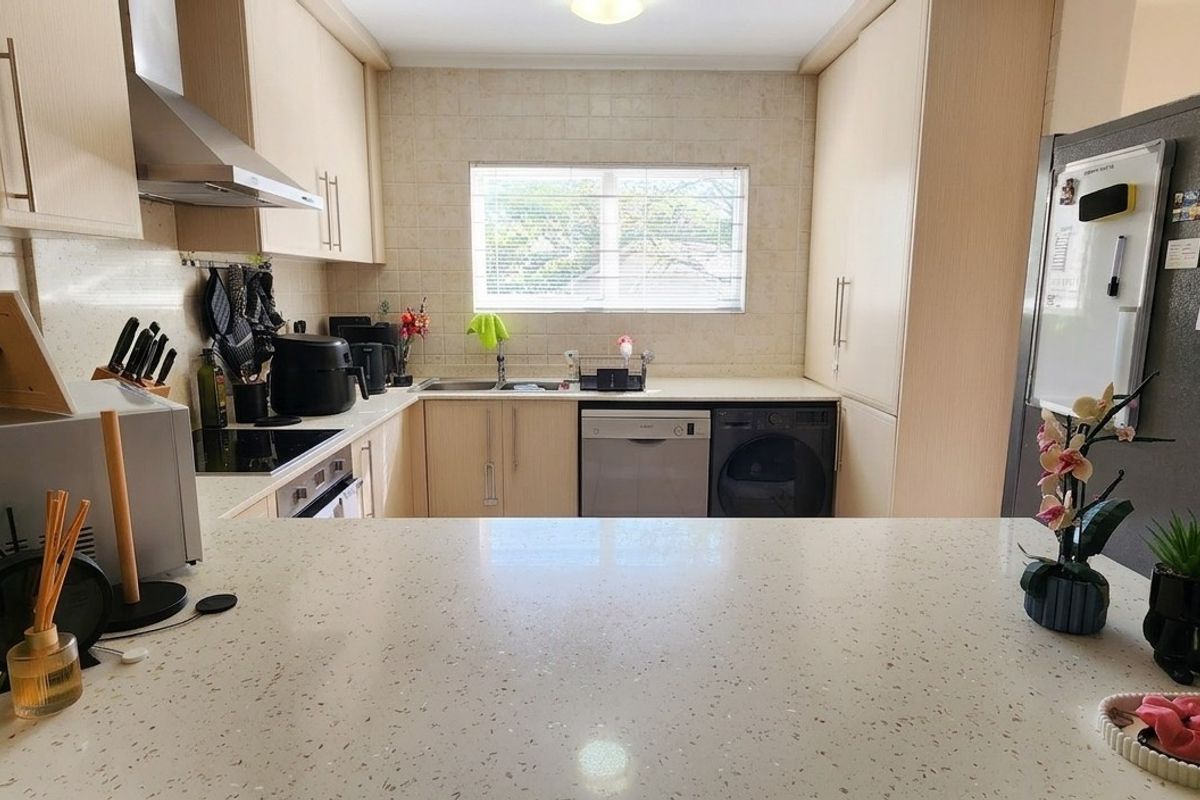 A functional kitchen featuring light-toned laminate cabinetry, stone countertops, a tiled backsplash, and integrated appliances, offering a clean and practical workspace.