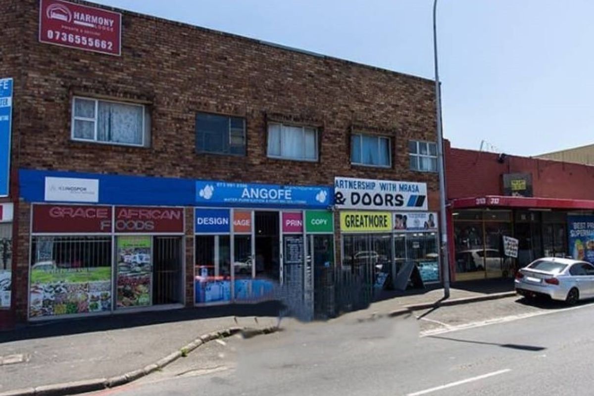 Street-level view of a multi-tenant commercial building featuring brick facade, large display windows, and various business signage along the main road.