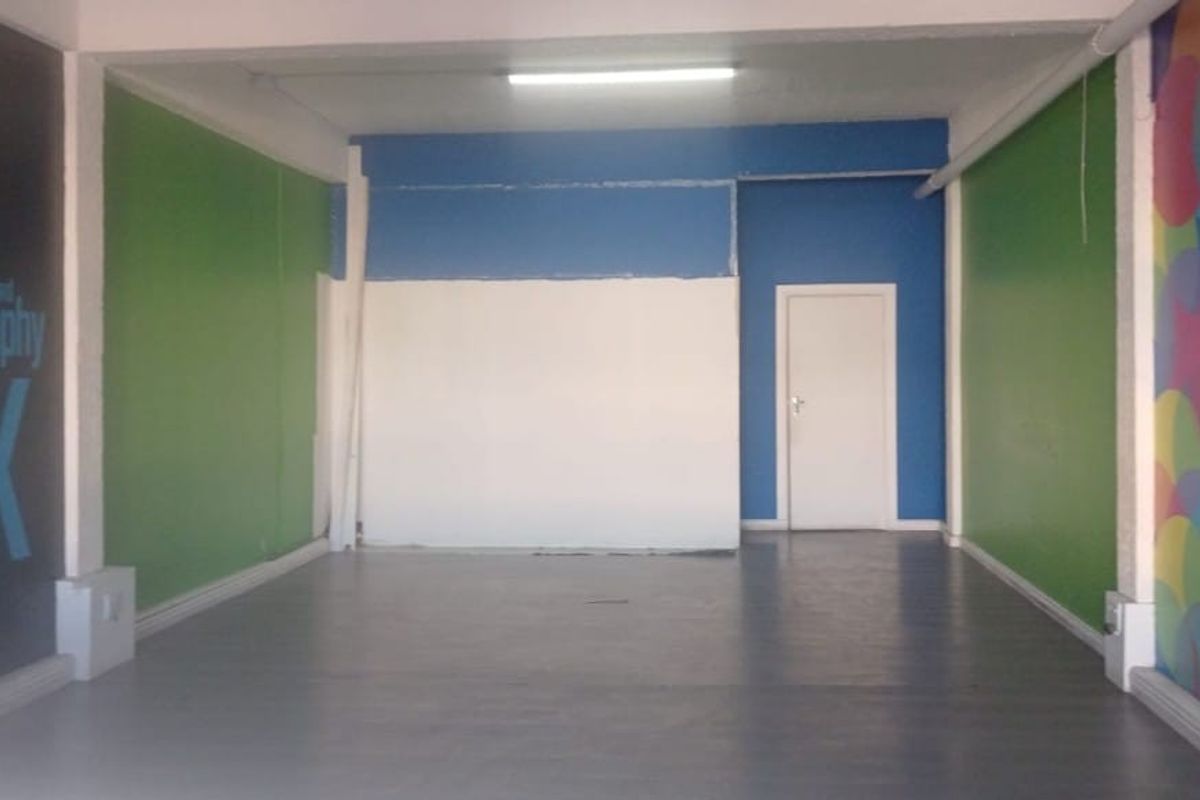 An open-plan commercial space featuring painted walls, grey flooring, and a single internal door, suitable for a variety of business or retail uses.