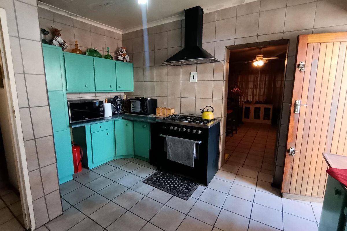 A functional kitchen featuring teal cabinetry, tiled walls and flooring, and a black freestanding gas stove with a matching extractor fan.