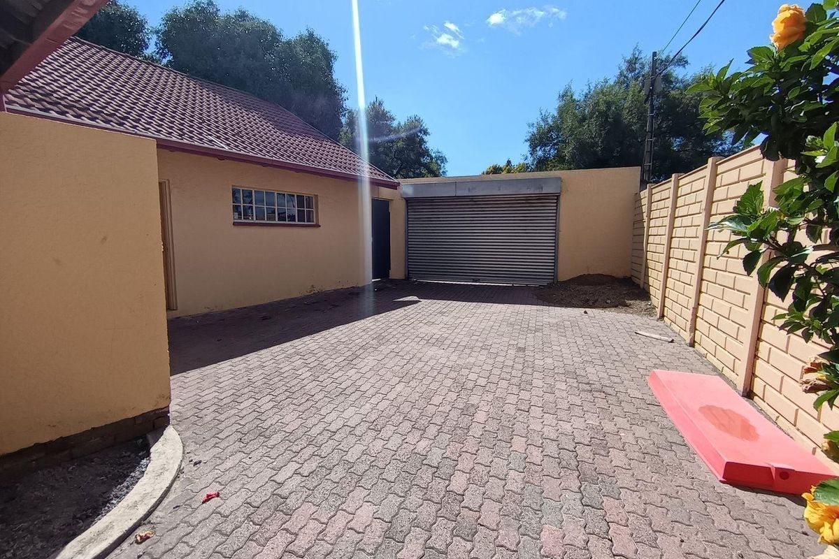 A paved driveway area featuring a secure roller shutter garage door, enclosed by perimeter boundary walls and a tiled roof structure.