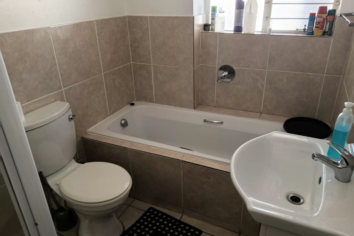 A functional bathroom featuring a built-in bathtub, ceramic wall tiling, a standard toilet, and a pedestal washbasin with chrome fixtures.