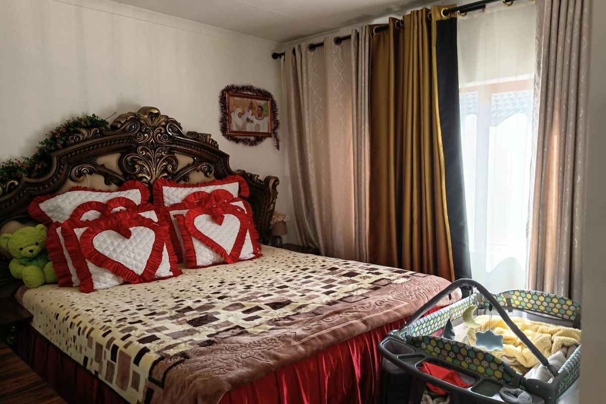 A bedroom featuring laminate flooring and large window treatments, providing a functional space for rest.