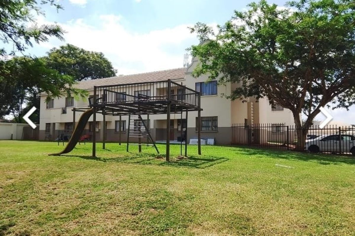 Exterior view of the apartment complex featuring a communal garden area with established trees and playground equipment.
