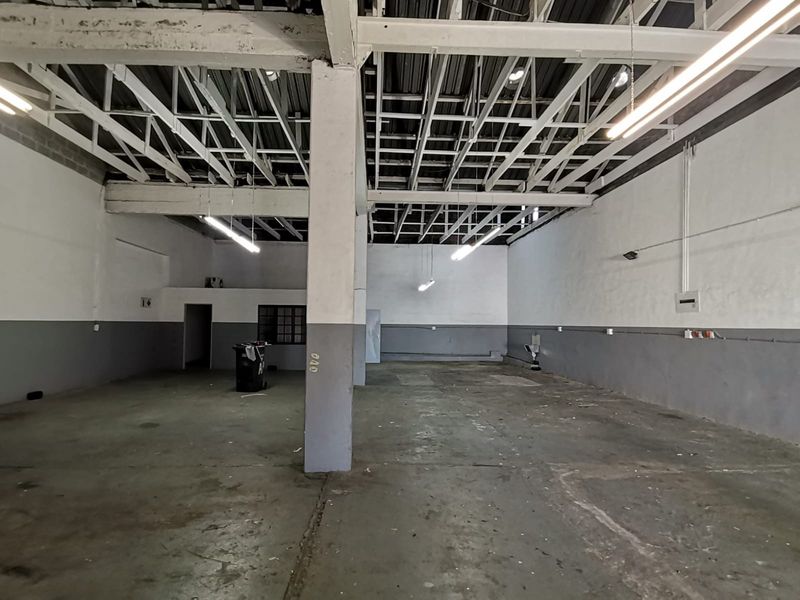 Spacious industrial utility space featuring exposed steel roof trusses, concrete flooring, and functional industrial lighting, suitable for workshop or storage use.