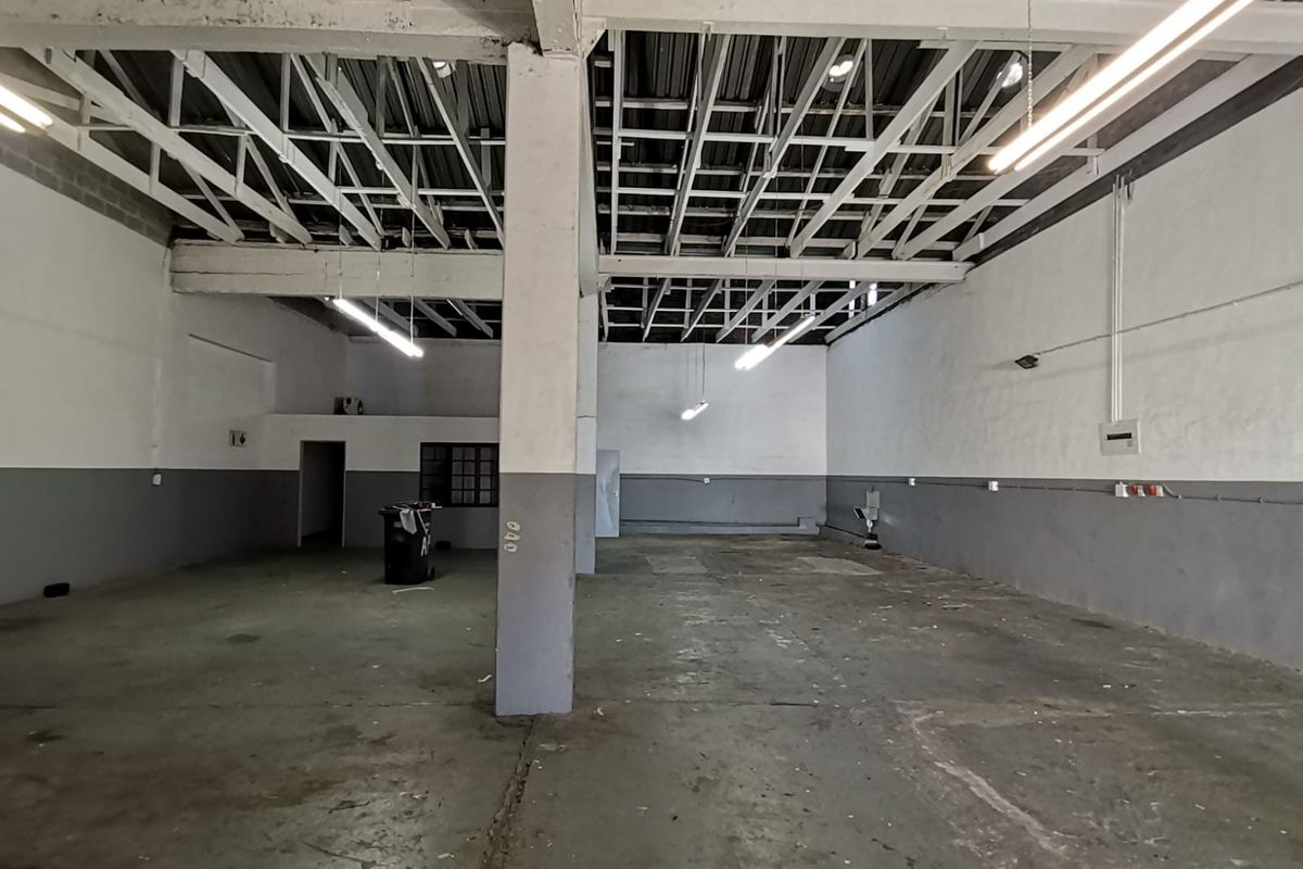 Spacious industrial utility space featuring exposed steel roof trusses, concrete flooring, and functional industrial lighting, suitable for workshop or storage use.