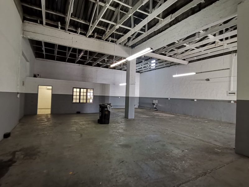 Spacious industrial utility area featuring exposed roof trusses, concrete flooring, and functional strip lighting, suitable for workshop or storage use.