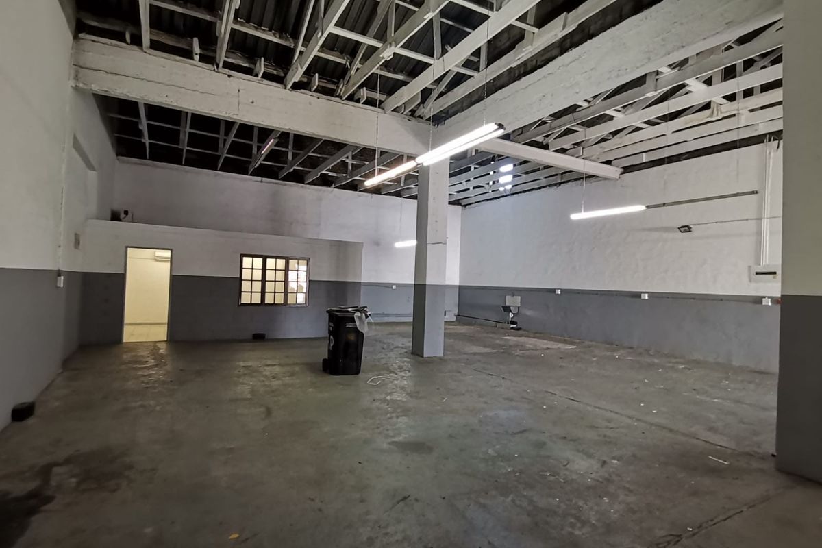 Spacious industrial utility area featuring exposed roof trusses, concrete flooring, and functional strip lighting, suitable for workshop or storage use.