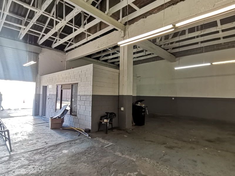 Spacious industrial utility area featuring exposed steel roof trusses, concrete flooring, and a roller shutter door, suitable for workshop or storage use.