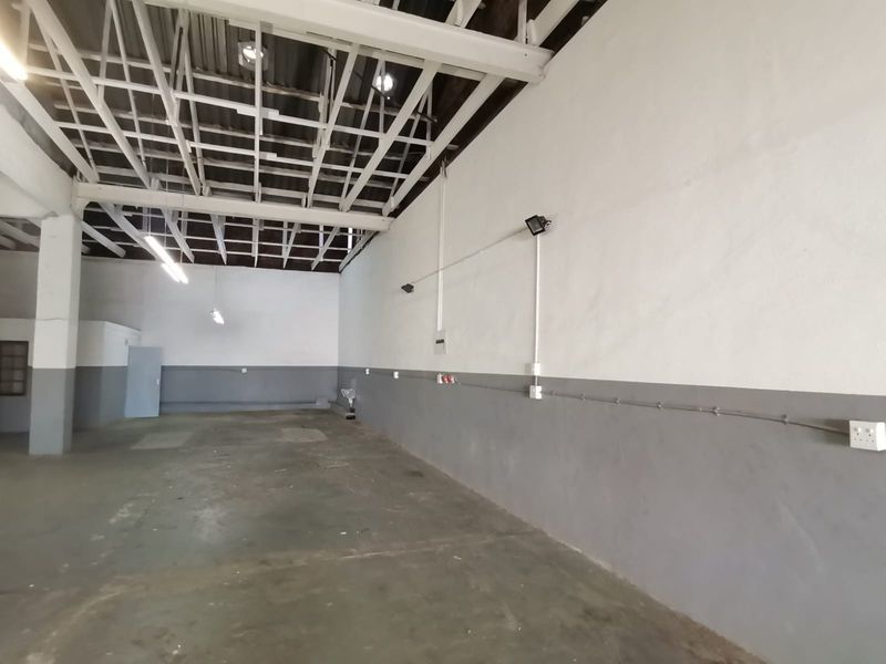Spacious industrial utility area featuring exposed steel roof trusses, concrete flooring, and surface-mounted electrical infrastructure, suitable for storage or workshop use.
