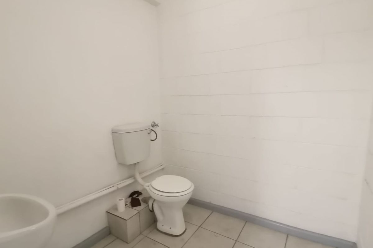 A functional, minimalist bathroom featuring a standard toilet, tiled flooring, and exposed plumbing fixtures in a simple industrial-style setting.