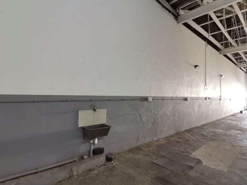 Spacious industrial utility area featuring exposed steel roof trusses, concrete flooring, and a wall-mounted utility sink with surface-mounted electrical infrastructure.