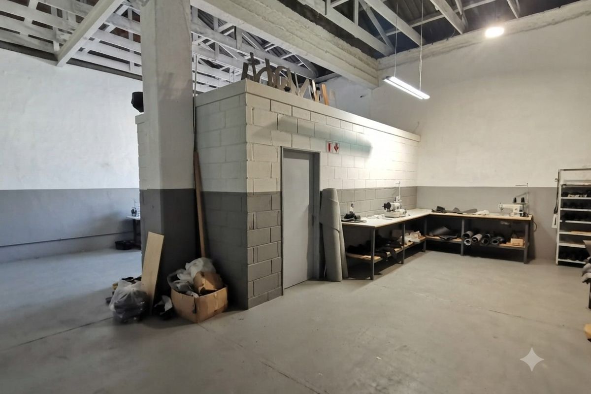 Spacious industrial workshop area featuring high exposed ceilings, concrete flooring, and a partitioned utility room with built-in workbench space.