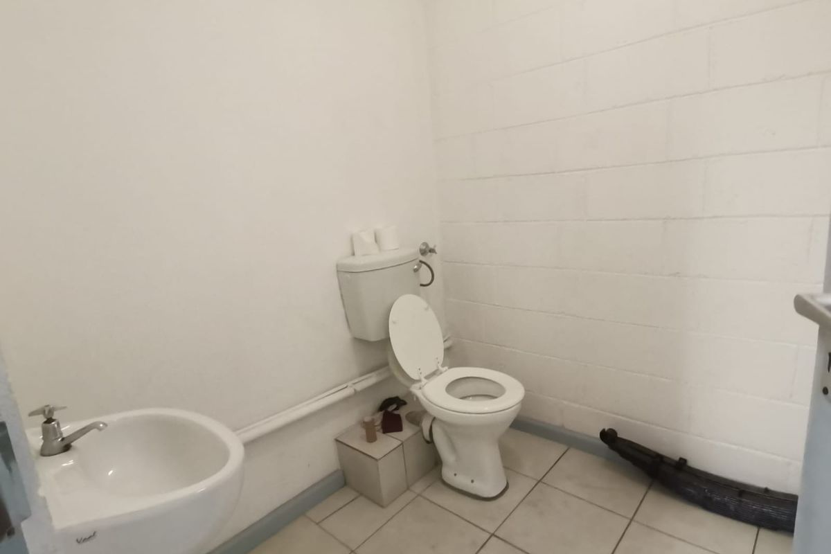 A functional industrial-style restroom featuring a standard toilet and wall-mounted basin with exposed plumbing and painted blockwork walls.