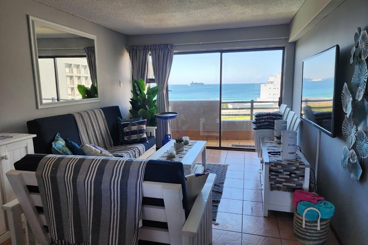 A bright living room featuring large sliding glass doors that open to a balcony with scenic ocean views.