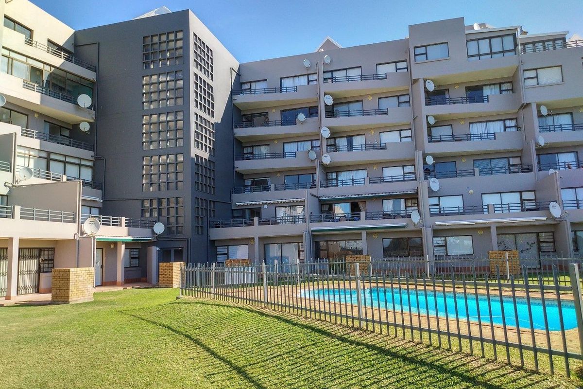 Exterior view of a multi-story apartment complex featuring a communal swimming pool, fenced garden area, and private balconies for each unit.