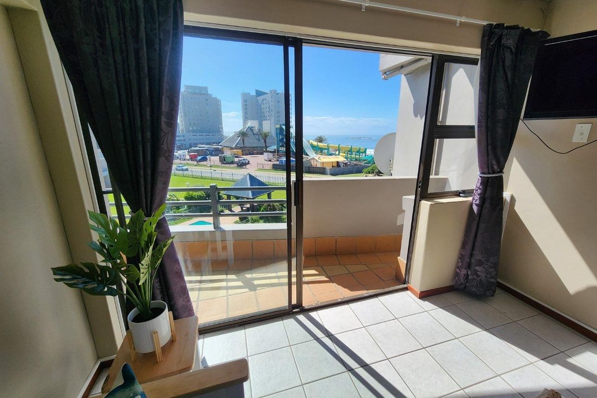 A bright living area featuring large sliding glass doors that open onto a private balcony with scenic coastal and urban views.