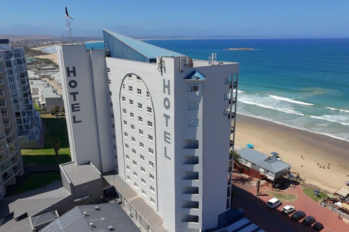 Aerial view of a multi-story hotel building situated directly on the beachfront, showcasing its prominent coastal location and proximity to the ocean.