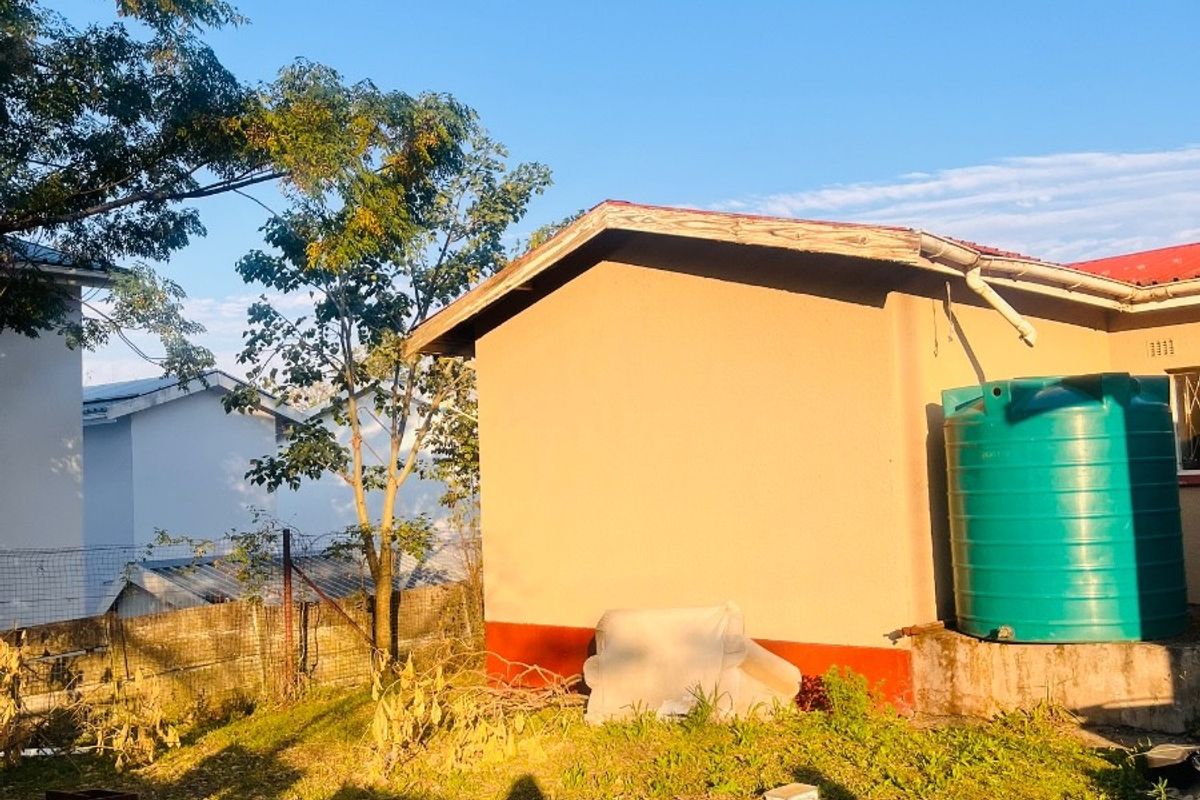 Rear exterior view of the property featuring a side wall, a large green water storage tank, and a grassed backyard area.