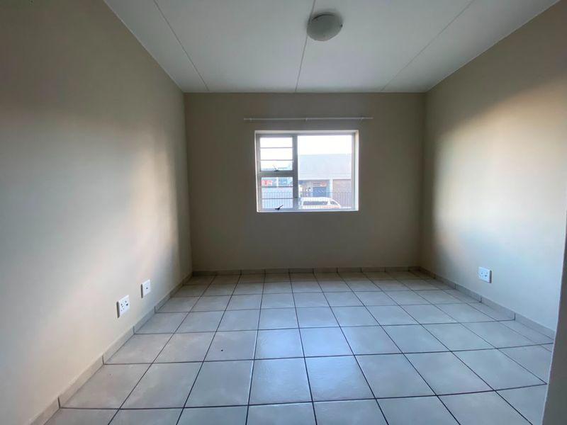 A clean, empty bedroom featuring neutral tiled flooring, a window with security bars, and standard electrical fixtures.