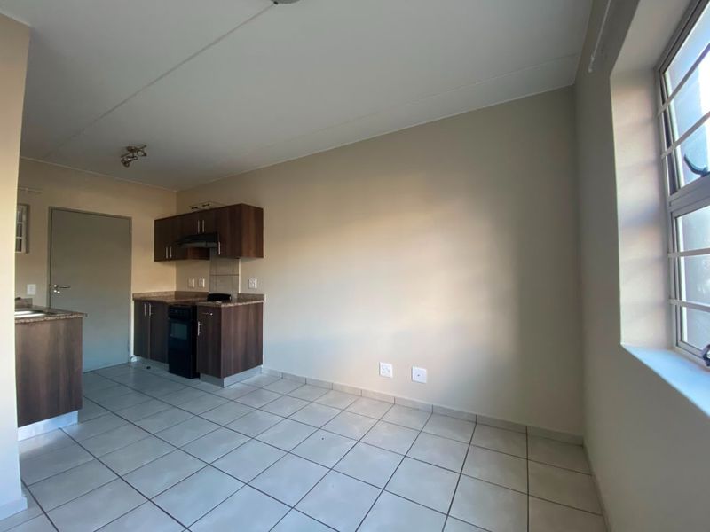An open-plan living and kitchen area featuring tiled flooring, built-in cabinetry, and a window with security bars.