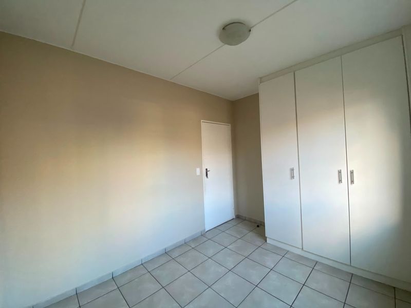 A clean, empty bedroom featuring neutral wall paint, tiled flooring, and built-in white cupboards, offering a blank canvas for personalization.