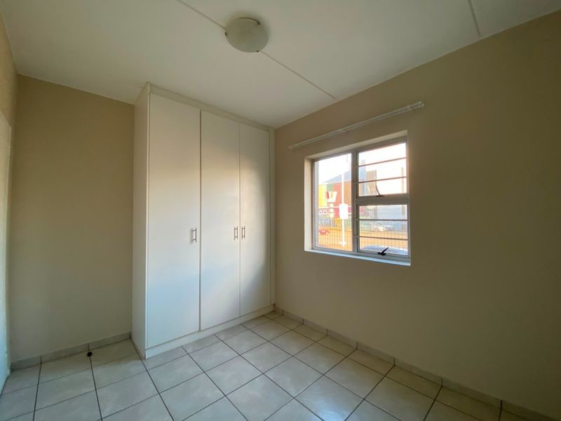 A clean, empty bedroom featuring neutral wall paint, tiled flooring, and a built-in white wardrobe with ample storage space.