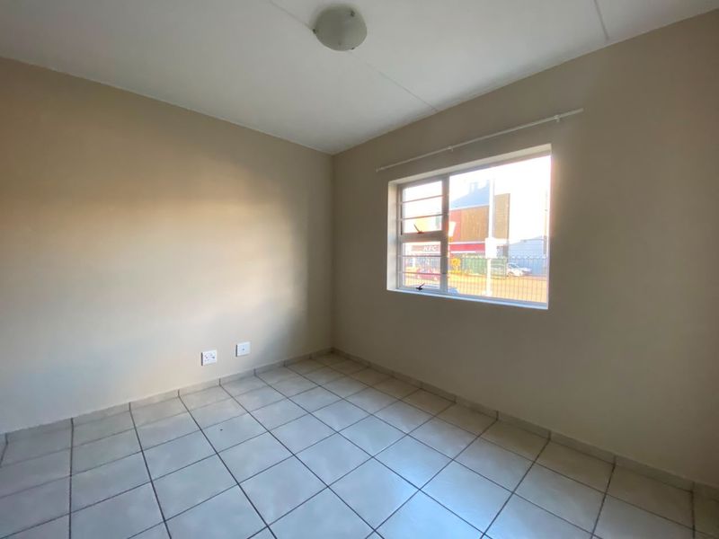A vacant bedroom featuring neutral wall paint, tiled flooring, and a window fitted with security bars.