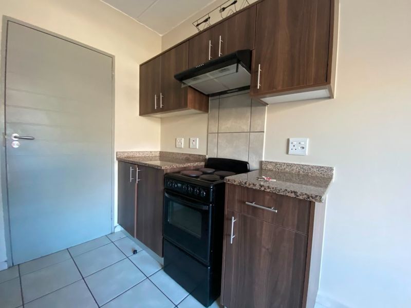 A compact kitchen featuring dark wood-look cabinetry, granite countertops, a tiled splashback, and an integrated extractor fan.