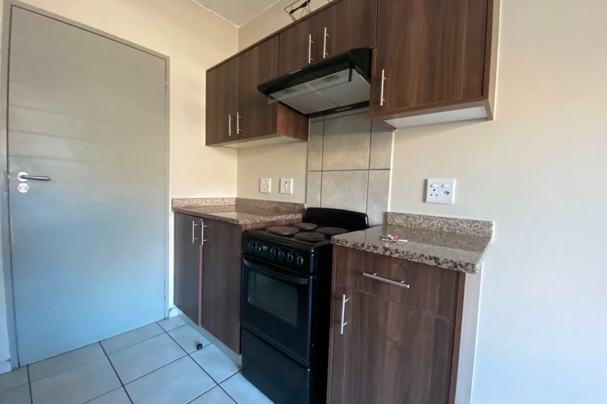 A compact kitchen featuring dark wood-look cabinetry, granite countertops, a tiled splashback, and an integrated extractor fan.