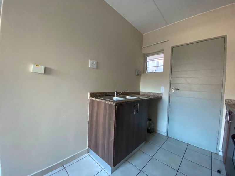 A compact kitchen area featuring dark wood-finish cabinetry, a double sink with a mixer tap, tiled flooring, and a louvered window.