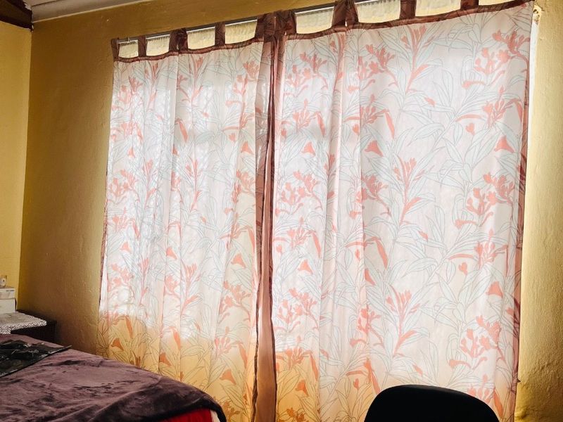 A bedroom featuring timber ceiling accents and a window with curtain fixtures, requiring cosmetic updates to the wall and ceiling finishes.