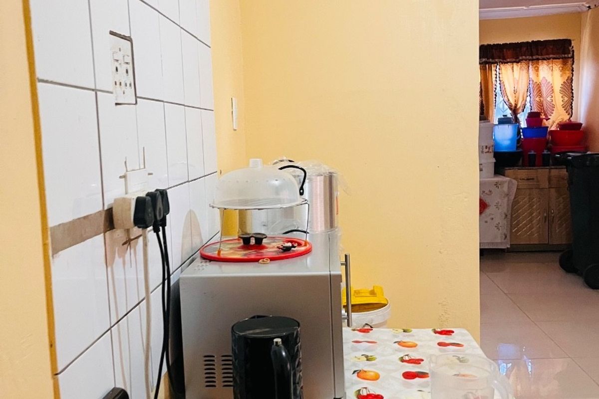 A compact kitchen area featuring a tiled splashback, electric stove, and visible wall cracking, requiring maintenance and cosmetic updates.