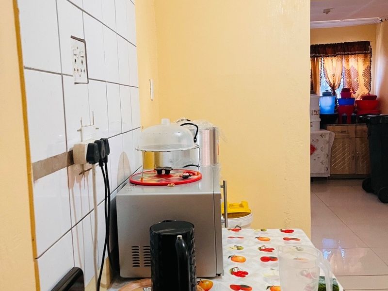 A compact kitchen area featuring a tiled splashback, electric stove, and visible wall cracking, requiring maintenance and cosmetic updates.