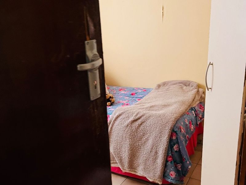 A view into a bedroom featuring tiled flooring and visible wall damage, captured through a partially open doorway.