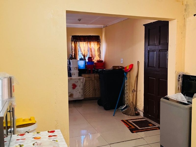 A functional scullery or utility area featuring tiled flooring and direct access to an adjacent room, showing signs of wear and maintenance requirements.
