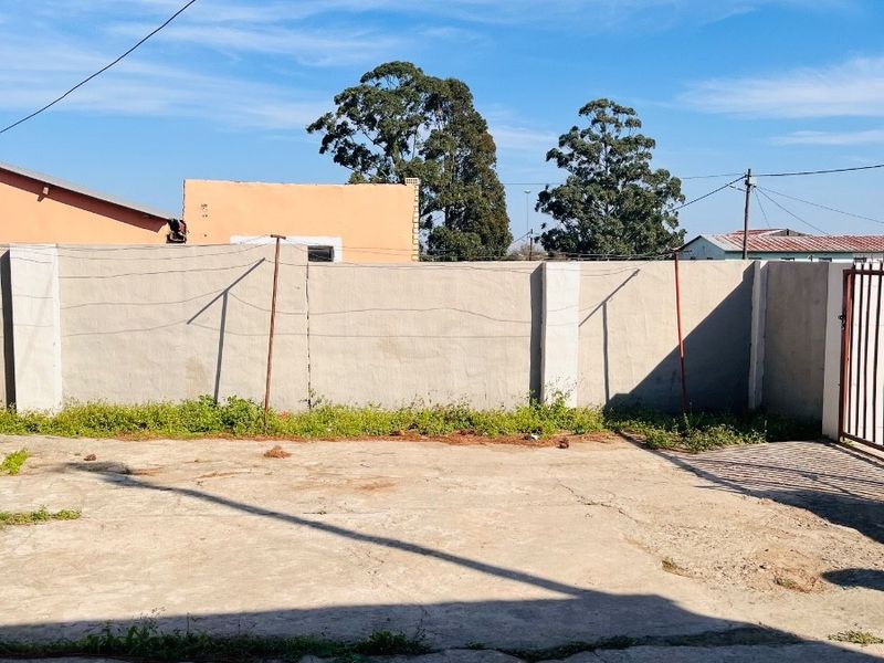 A paved outdoor yard area featuring a perimeter boundary wall with integrated metal gate and overhead utility lines.