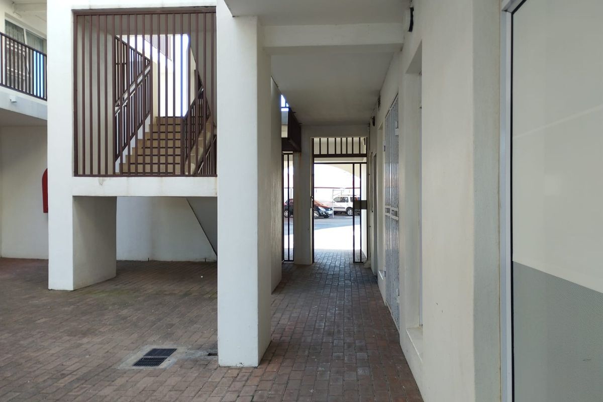 A covered outdoor walkway and communal area featuring brick paving, structural pillars, and a metal staircase leading to upper levels.