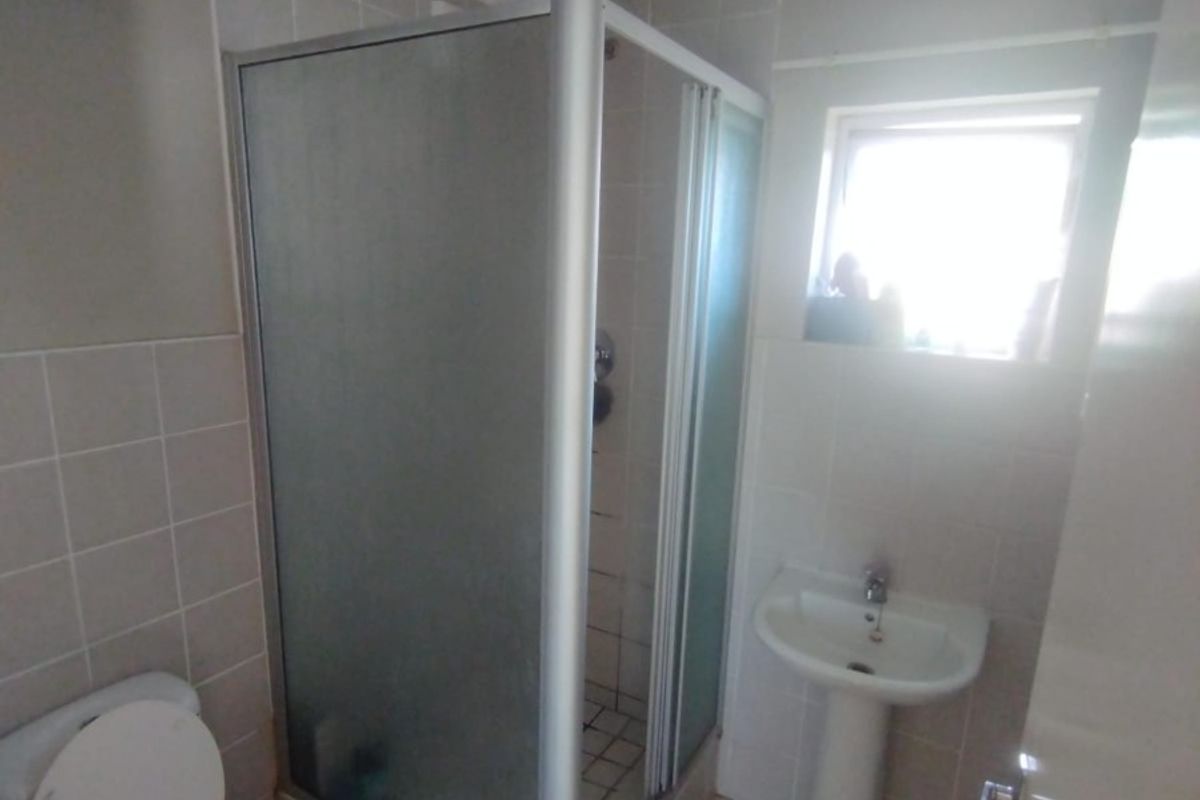 A functional bathroom featuring a corner shower enclosure, pedestal basin, and toilet with neutral wall and floor tiling.