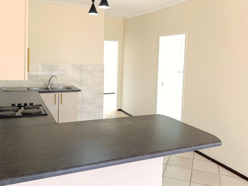 A functional kitchen featuring built-in cabinetry, a dark laminate countertop, a built-in hob, and tiled flooring in an open-plan layout.