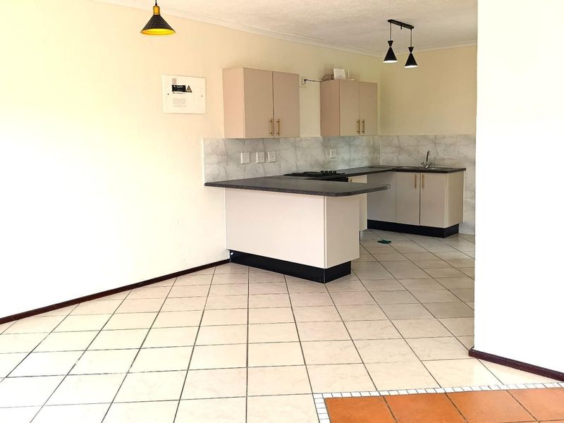 An open-plan kitchen area featuring neutral cabinetry, laminate countertops, tiled flooring, and a tiled backsplash, offering a clean and functional space.