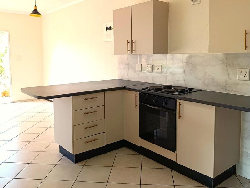 A functional kitchen featuring built-in cabinetry, dark laminate countertops, an integrated electric hob and oven, and a tiled backsplash, opening into a living area.
