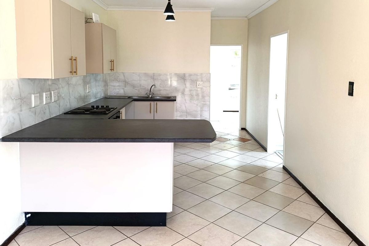 A clean, empty kitchen featuring built-in cabinetry, laminate countertops, a gas hob, and tiled flooring, offering a functional space ready for personalization.