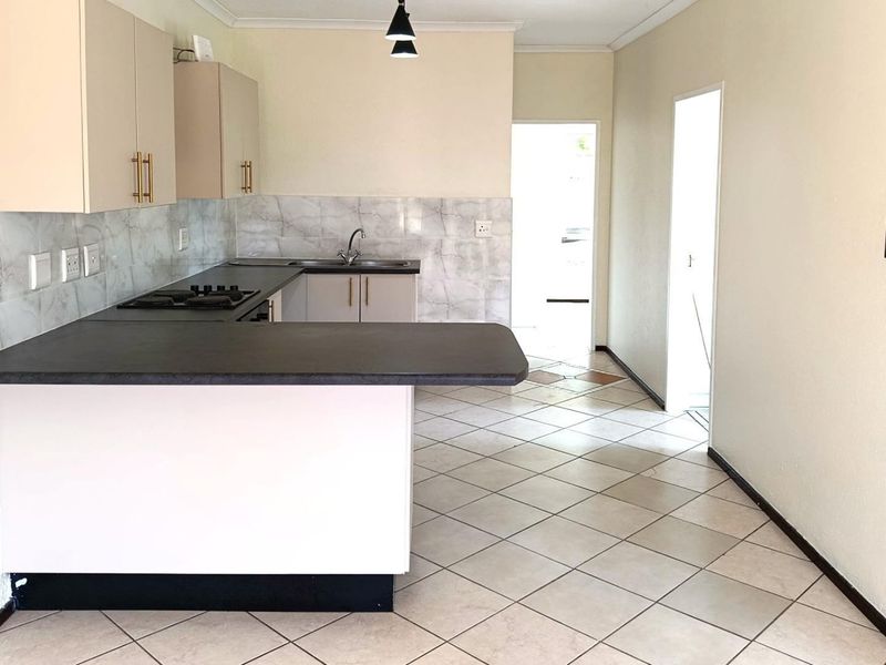 A clean, empty kitchen featuring built-in cabinetry, laminate countertops, a gas hob, and tiled flooring, offering a functional space ready for personalization.