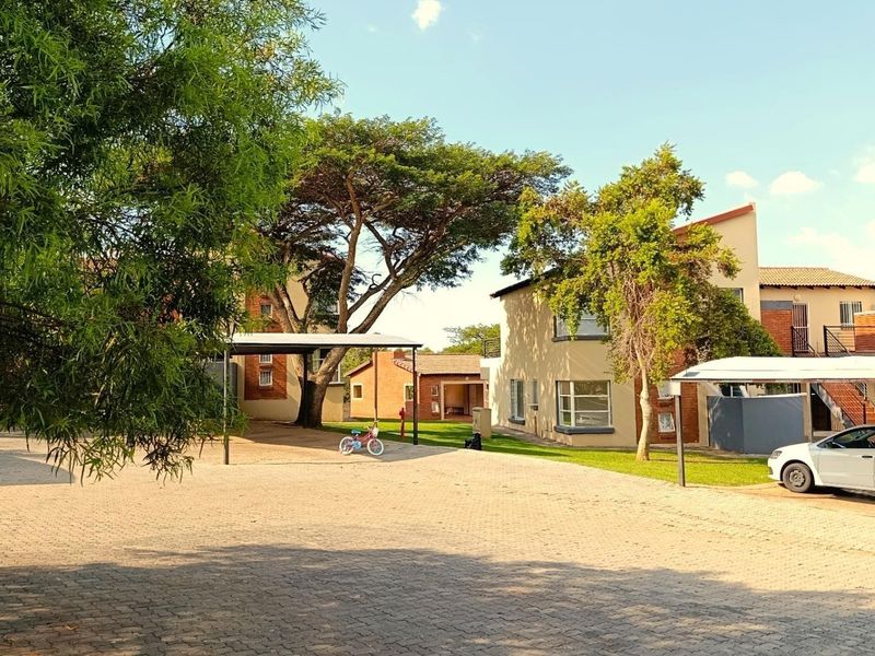 Exterior view of the apartment complex featuring paved parking areas, covered carports, and established garden surroundings.