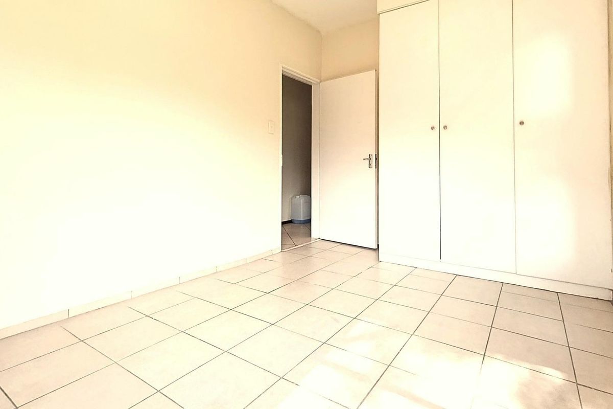 A bright, empty bedroom featuring neutral tiled flooring and built-in cupboards, offering a clean and versatile space ready for personalization.