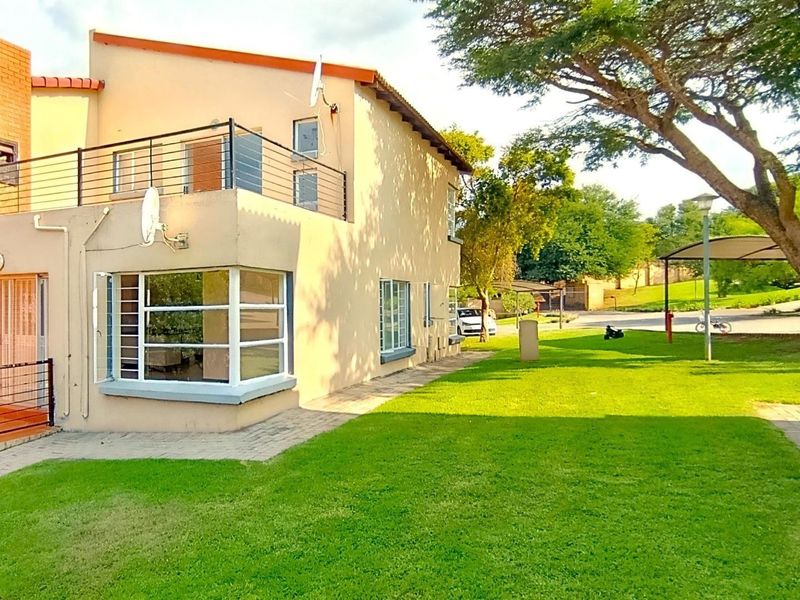 Rear view of the apartment building featuring a balcony with metal railings, a bay window, and access to a shared garden area.