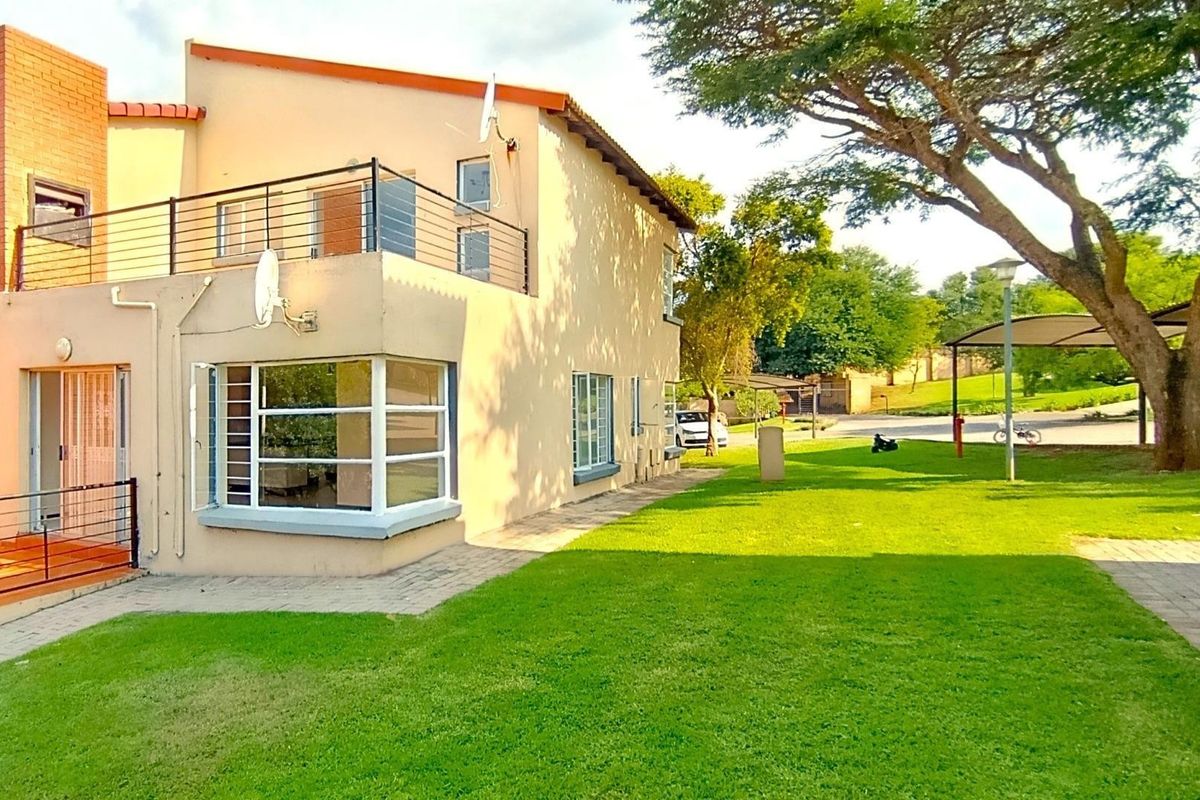 Rear view of the apartment building featuring a balcony with metal railings, a bay window, and access to a shared garden area.
